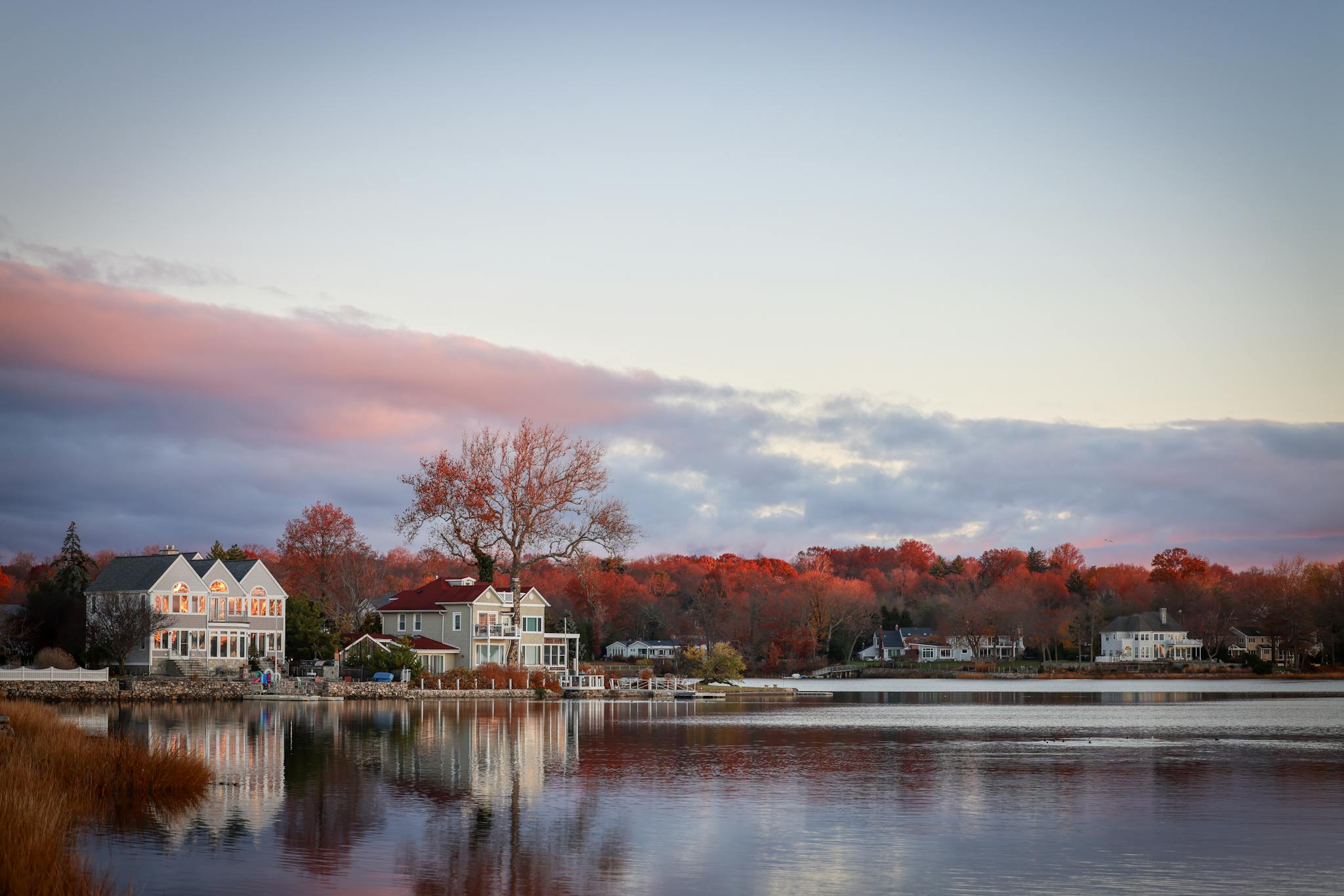 Picturesque autumn lake scene with houses and vibrant foliage under a dramatic sky.